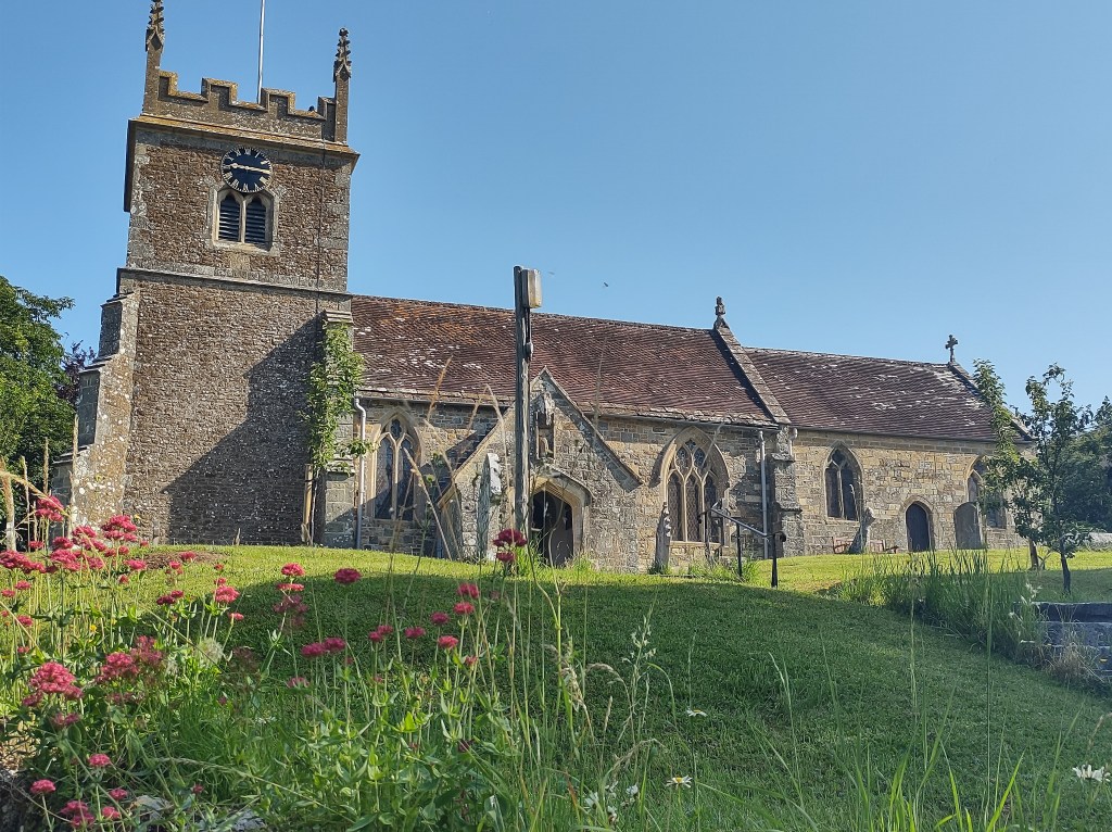 cozy image of a medieval English village church with flowers and grass around it